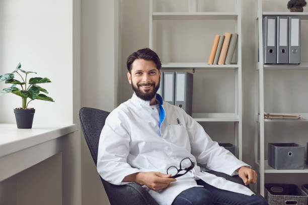 Portrait of smiling male doctor in medical office. Sitting comfortable in armchair, looking at camera. stock photo