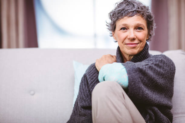 Portrait of smiling mature woman sitting on sofa Portrait of smiling mature woman sitting on sofa at home 55 59 years stock pictures, royalty-free photos & images