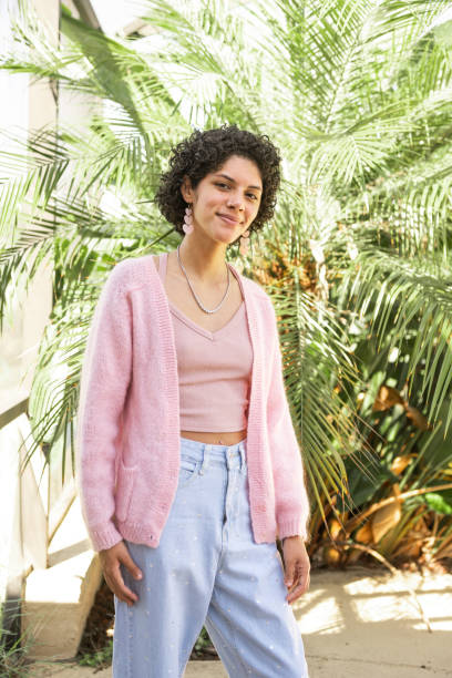 Portrait of Smiling Puerto Rican Woman by Palm Tree in Orlando This is a portrait of a young Hispanic Puerto Rican woman in her 20s standing outdoors by a palm tree in the backyard in Orlando, Florida. She has short curly hair and wears a pink sweater. puerto rican women stock pictures, royalty-free photos & images