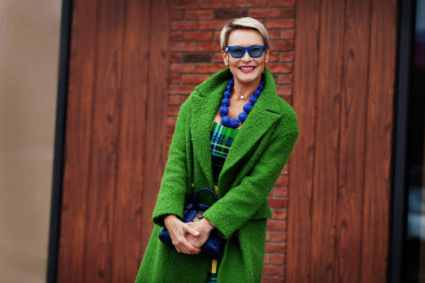 porträt einer lächelnden stilvollen frau in grünem mantel mit blauen accessoires. buntes trendiges casual-outfit. happy model 45-50 jahre alt mit kurzen modischen haarschnitt - women fashion stock-fotos und bilder