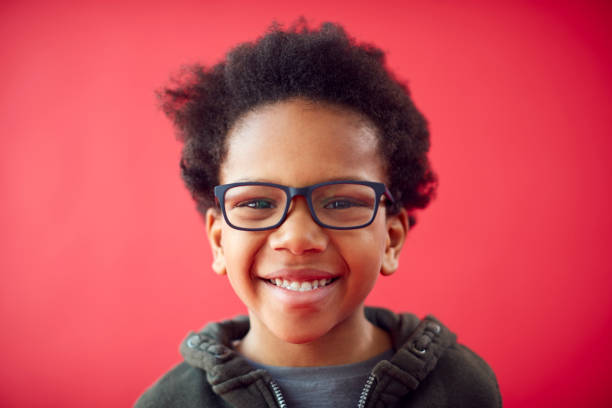porträt eines lächelnden jungen jungen, der eine brille vor rotem studiohintergrund trägt - 6 7 jahre stock-fotos und bilder