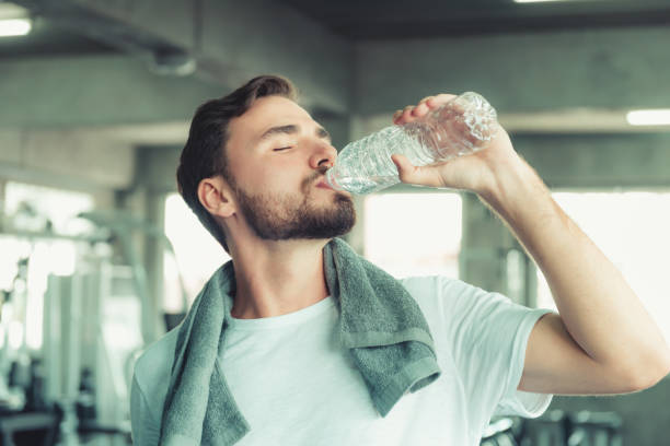 Portrait of Sport Man in Fitness Club and Drinking a Bottle of Water After Braking Exercised on Bodybuilding Equipment Background, Handsome Man is Relaxing While Exercising in Gym. Healthy/Fitness stock photo