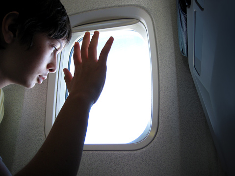 Teenage boy sitting on airplane window seat and looking out