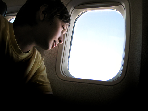 Teenage boy sitting on airplane window seat and looking out
