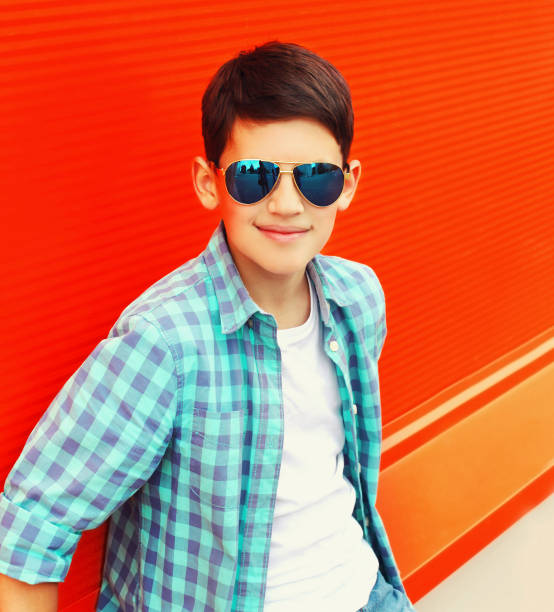 Portrait of teenager boy wearing sunglasses and shirt in the city on red background stock photo