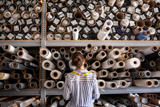 portrait of textile designer choosing fabric from stack of rolls inside sustainable workshop - duurzame stoffen stockfoto's en -beelden