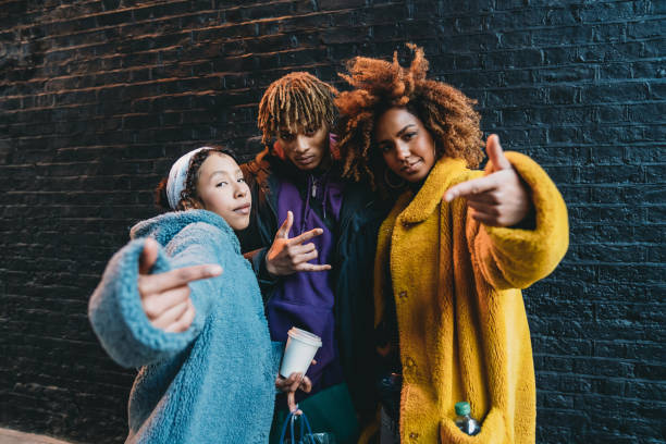 Portrait of three friends against a black bricks wall, making gestures in front of the camera Portrait of three friends against a black bricks wall, making gestures in front of the camera. They are wearing colorful and hip clothes. rapper stock pictures, royalty-free photos & images