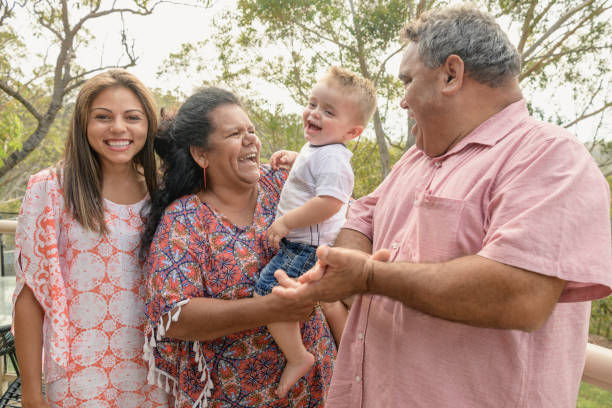 Portrait of three generation Aboriginal family Grandparents holding little boy, mother smiling towards camera, grandfather clapping australian culture stock pictures, royalty-free photos & images
