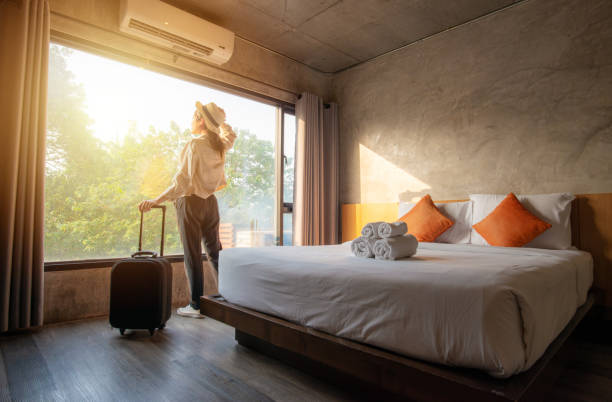 portrait of tourist woman standing nearly window, looking to beautiful view with her luggage in hotel bedroom after check-in. - hotel imagens e fotografias de stock