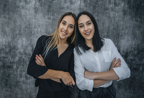 Portrait of two successful female twins businesswomen in suits on a gray background. Family, Global, Siblings, Sisters, Stills, Twins, girls