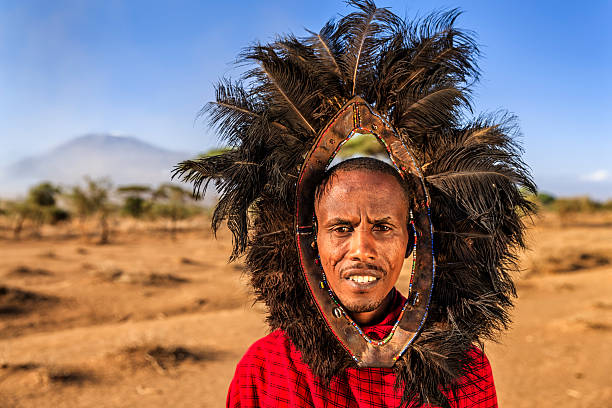 Portrait of warrior from Maasai tribe, Kenya, Africa African warrior from Maasai tribe wears an ostrich feather headdress  - Mount Kilimanjaro on the background, central Kenya, Africa. Maasai tribe inhabiting southern Kenya and northern Tanzania, and they are related to the Samburu. masai warrior stock pictures, royalty-free photos & images