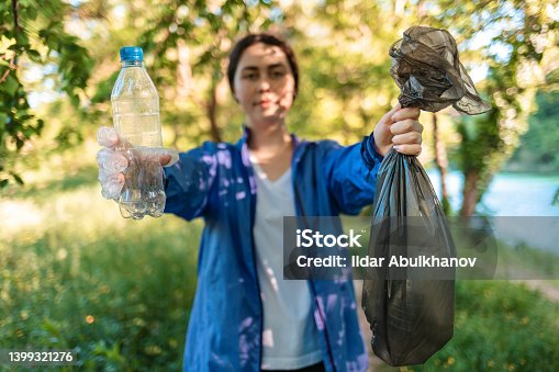 istock Portrait of woman in sportswear holding garbage of a bag and showing plastic bottle. The concept of environmental protection, plogging and volunteering 1399321276
