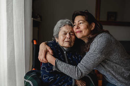 Portrait of woman in wheelchair hugging daughter with positive face. Third old age, Home care concept.