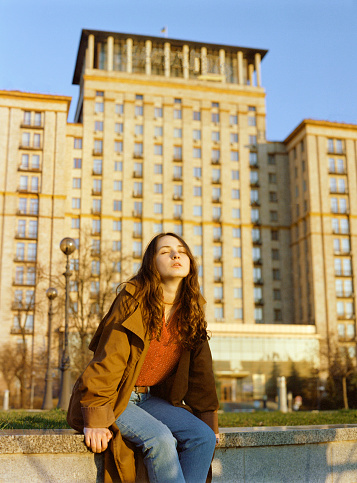 Portrait of  the young Caucasian woman in coat  standing on the background of Kyiv cityscape. Medium format film