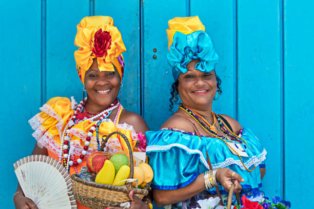 Portrait of women in Cuban traditional dresses Portrait of happy Cuban women standing against blue wooden wall. Smiling mature women are in traditional dresses. They are with fruit basket and hand fan. antilles stock pictures, royalty-free photos & images