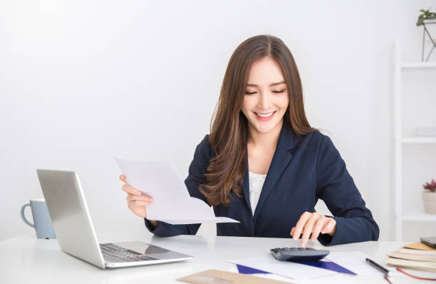 Portrait of young asian business woman paying bills online with laptop in office. Beautiful girl at desk with computer and chequebook, happy paying bills. Startup businesswoman financial calculating number bank account concept Portrait of young asian business woman paying bills online with laptop in office. Beautiful girl at desk with computer and chequebook, happy paying bills. Startup businesswoman financial calculating number bank account concept business girls stock pictures, royalty-free photos & images