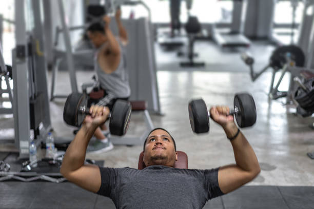Portrait of young Asian  man muscular built athlete  working out in gym, lying holding two dumbbell stock photo