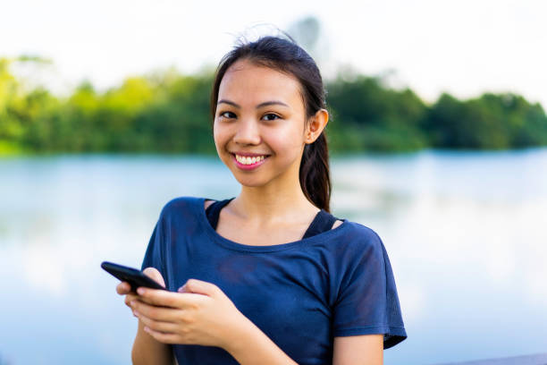 Portrait of young Asian woman by a lake Portrait of young Asian woman by a lake, using a mobile phone filipino ethnicity stock pictures, royalty-free photos & images