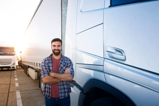 Portrait of young bearded man standing by his truck. Professional truck driver with crossed arms standing by semi truck vehicle. Portrait of young bearded man standing by his truck. Professional truck driver with crossed arms standing by semi truck vehicle. truck driver stock pictures, royalty-free photos & images