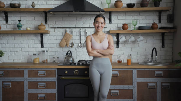 porträtt av ung vacker asiatisk kvinna som står vid köket, tittar på kameran och ler - slow motion bildbanksfoton och bilder