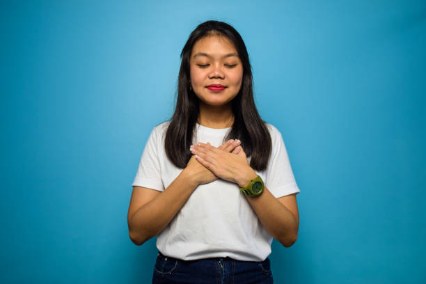 Portrait of Young beautiful asian women using white T-shirt with blue isolated background Portrait of Young beautiful asian women using white T-shirt with blue isolated background, smiling with hands on chest with closed eyes and grateful indonesian woman stock pictures, royalty-free photos & images