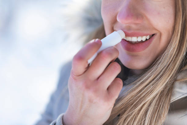 Portrait of young female applying lip balm in winter. Portrait of young female applying lip balm in winter. Portrait of a beautiful woman in snow with application of the protective cream to the lips human lips stock pictures, royalty-free photos & images