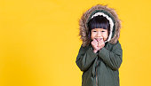 コピースペースで黄色の背景に隔離された毛皮のフード付き冬のコートセーターを着て若い幸せな小さなアジアの女の子の肖像画。教育幼年時代のライフスタイル、冬の冷たいバナー