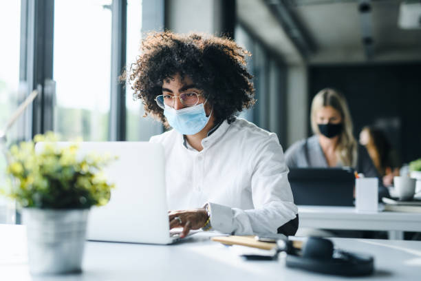 portrait of young man with face mask back at work in office after lockdown. - working office imagens e fotografias de stock