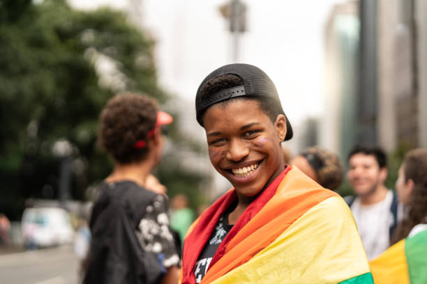 ゲイパレードで背景に友達と虹色の旗を持つ若者の肖像 - lgbtqiaの文化 ストックフォトと画像