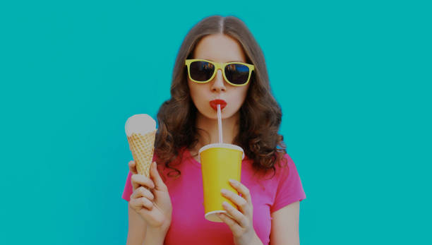 Portrait of young woman drinking a juice and holding ice cream on a blue background stock photo