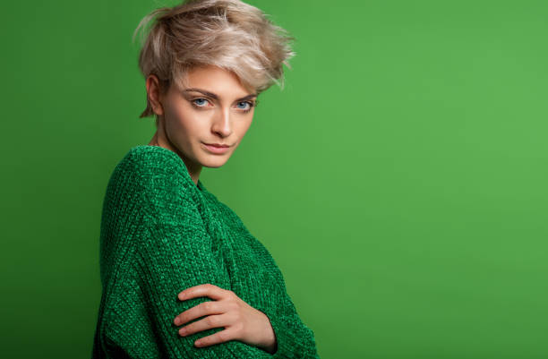 Portrait of young woman in blonde short hair wear green sweater isolated over green background stock photo