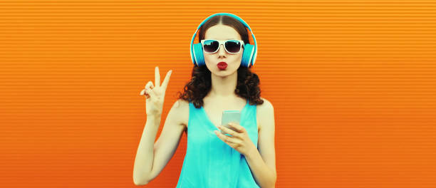 Portrait of young woman in headphones listening to music with smartphone on orange background stock photo