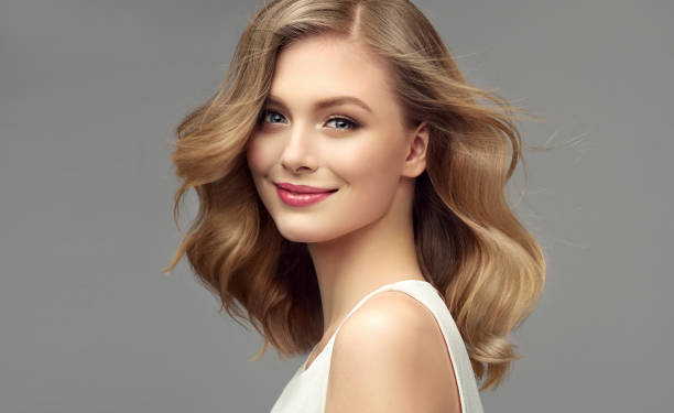 Portrait of young woman with dark blonde hair. Cosmetology, hairdressing and makeup. Model with dark blonde hair. Frizzy, elegant hairstyle is surrounding lovely face of tenderly smiling young woman. Natural gloss and softness of healthy hair. Hair care and hairdressing art. female likeness stock pictures, royalty-free photos & images