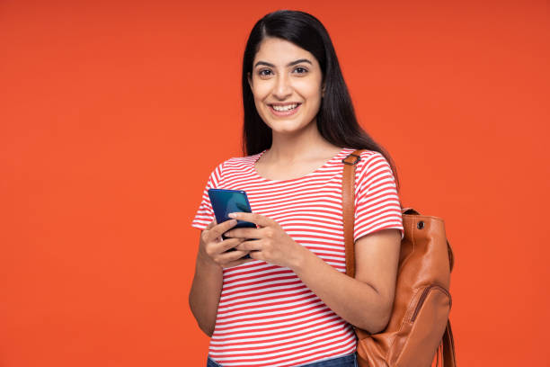 Portrait of young women student using mobile phone standing isolated over red background:- stock photo stock photo