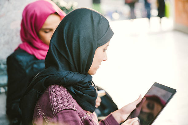 Portrait Of Young Women Wearing Headscarf Reading Books Outdoors stock photo