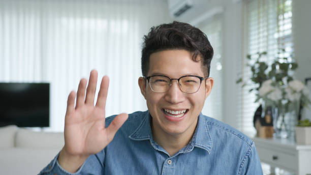 Portrait or headshot of young adult asian handsome man or model wearing eye glasses with cool hair big smiling confident and looking to camera with feeling happy and positive in living room at home.  wave goodbye asian stock pictures, royalty-free photos & images
