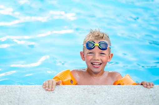 Portrait smiling boy in swimming pool, child in swimming glasses and inflatable sleeves. Summer travel hotel vacation or classes