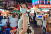 Portrait young cheerful Asian woman wearing facemask protection covid-19 virus outbreak in Chinatown at night , new normal travel concept ,Yaowarat Road Chinatown Bangkok