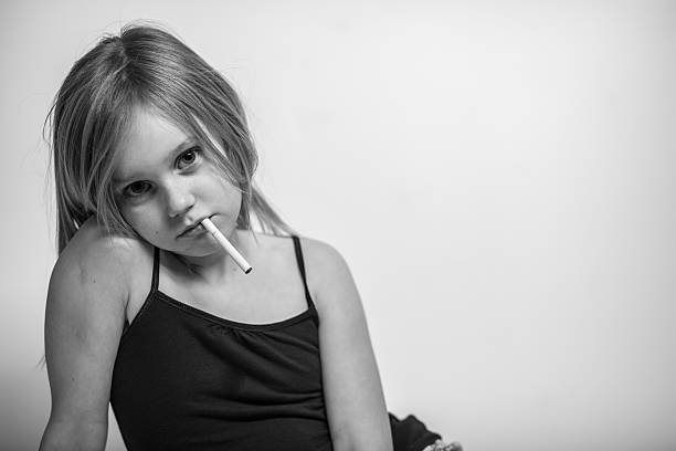 Portrait, Young Girl with Cigarette in Mouth, Black and White "Portrait of a young girl leaning listlessly on one arm, her head resting on her shoulder, an unlit cigarette dangling from her mouth. Black and white." little girl smoking cigarette stock pictures, royalty-free photos & images