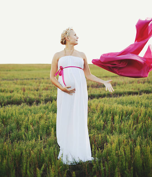 Portrat of young pregnant woman in a white greek dress outside.