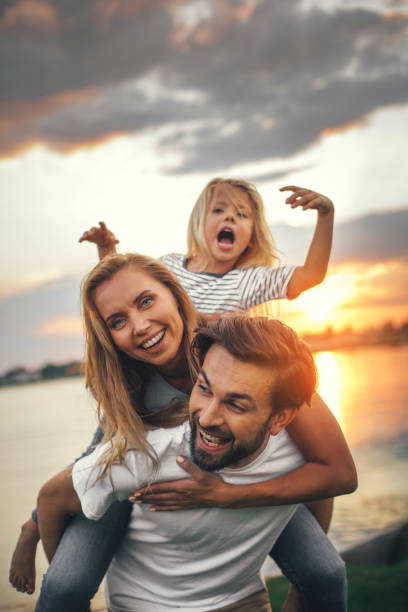 Positive parents having fun with glad daughter Portrait of happy unshaven husband spending tie with cheerful wife and satisfied female child in nature river photos stock pictures, royalty-free photos & images