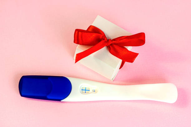 Positive pregnancy test with gift box on light pink background. Baby birth planning and child waiting concept stock photo
