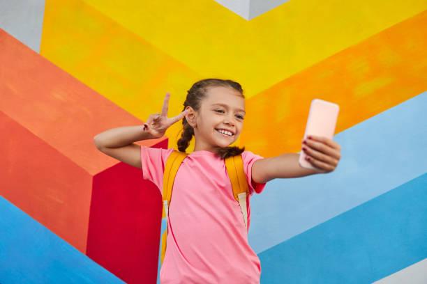 Positive schoolgirl taking selfie on smartphone stock photo