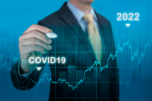 Post covid-19 economic recovery in 2022 concept. businessman hand with marker pointing graph growth plan on blue background. timeline chart diagram of global economic after crisis by covid19 pandemic