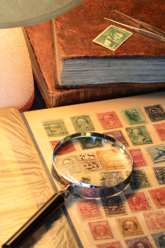 Closeup of a senior man's hand examining an old stamp book with magnifying glass