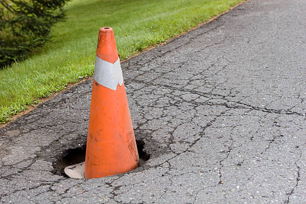 Pot hole in the road with an orange cone inside stock photo