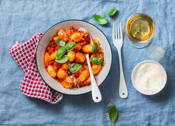 Potato gnocchi in tomato sauce with basil and parmesan and a glass of white wine on blue background, top view. Italian cuisine. Vegetarian food stock photo