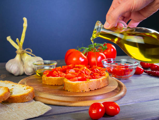 Pour olive oil on the food. Mediterranean food, Italian bruschetta with ingredients: bread, tomato, garlic and olive oil. Still life food. Hand holds bottle of extra virgin olive oil. stock photo