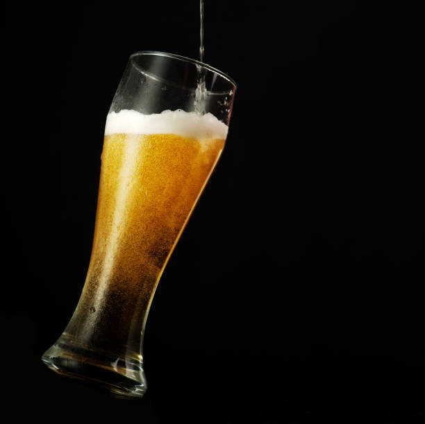 Pouring beer into glass over black background. stock photo