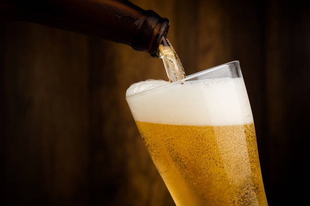 ボトルから冷たいビールを木の壁裏返しのアルコールのお祝いのコンセプトにガラスに注ぐ - ビール ストックフォトと画像